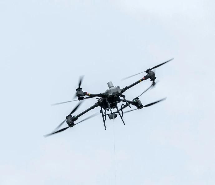 A drone flies against a cloudy sky.